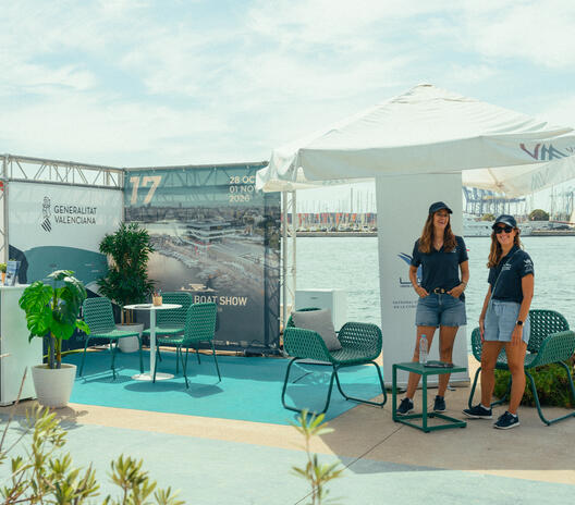 The brands, teams and spaces behind the event — Valencia Boat Show’s stand at SailGP. Two team members at the Valencia Boat Show stand, with branded displays, seating and plants beside the marina.