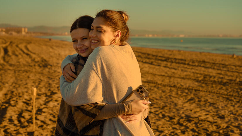Connection after the experience — Sync Club Two women embracing on the beach in warm early-morning light