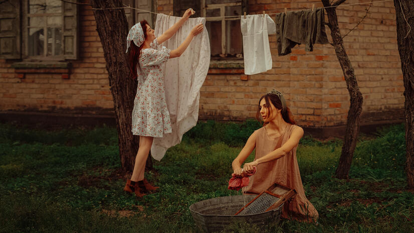 Styled campaign production Two women performing a vintage-inspired outdoor laundry scene beside a brick building