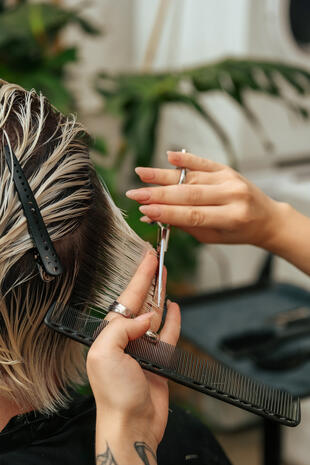 The precision and tactile detail behind the finished look. Close-up of a hairstylist’s hands cutting wet blonde hair with scissors and a black comb.