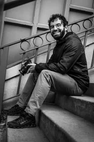 Creative professional behind the camera Smiling photographer seated on outdoor steps and holding a professional camera