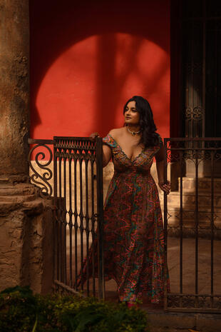 Portrait in the evening city Woman in a floral dress standing beside a metal gate and a warmly lit wall at night