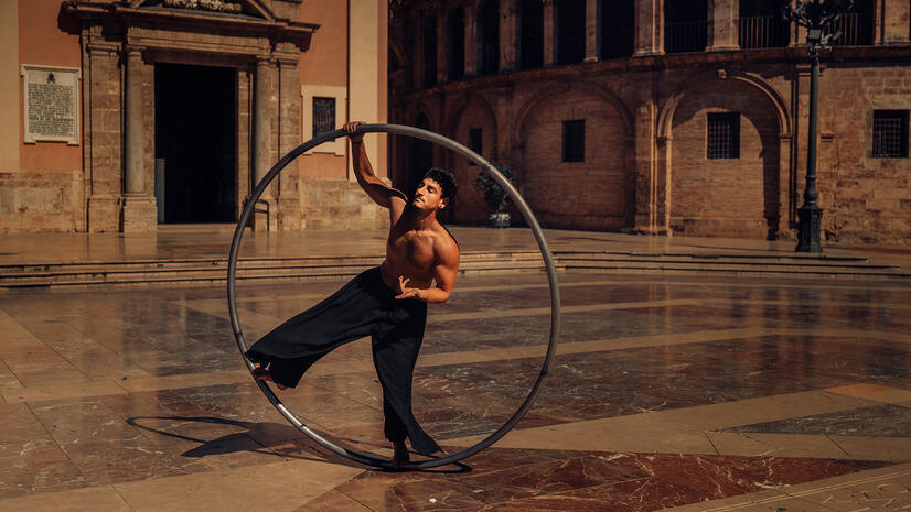 Movement in the city Circus performer balancing inside a large metal Cyr wheel in a historic city square