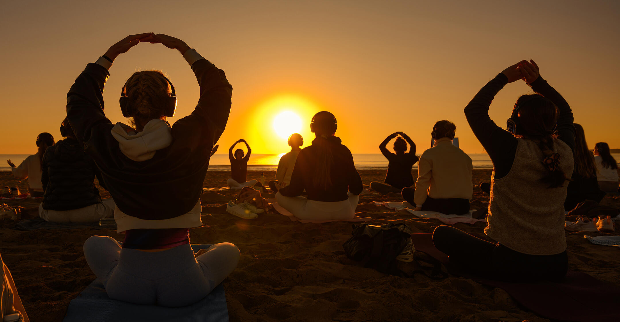 Collective breathwork at sunrise — Sync Club Group breathwork session on a beach at sunrise, with participants seated around the rising sun
